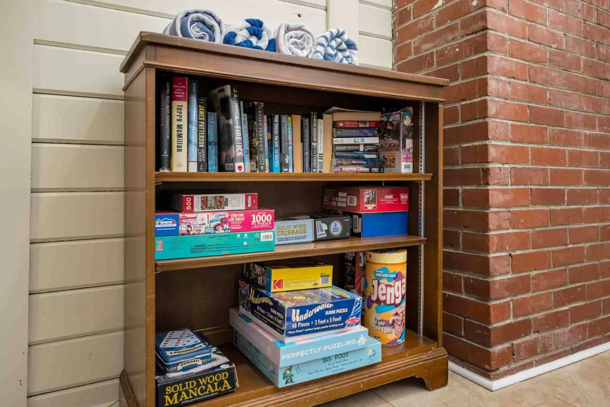 A cozy room with a bookshelf filled with board games and towels. The intimate setting hints at a space designed for both lively group activities and quiet moments, perfect for game nights or reading sessions.