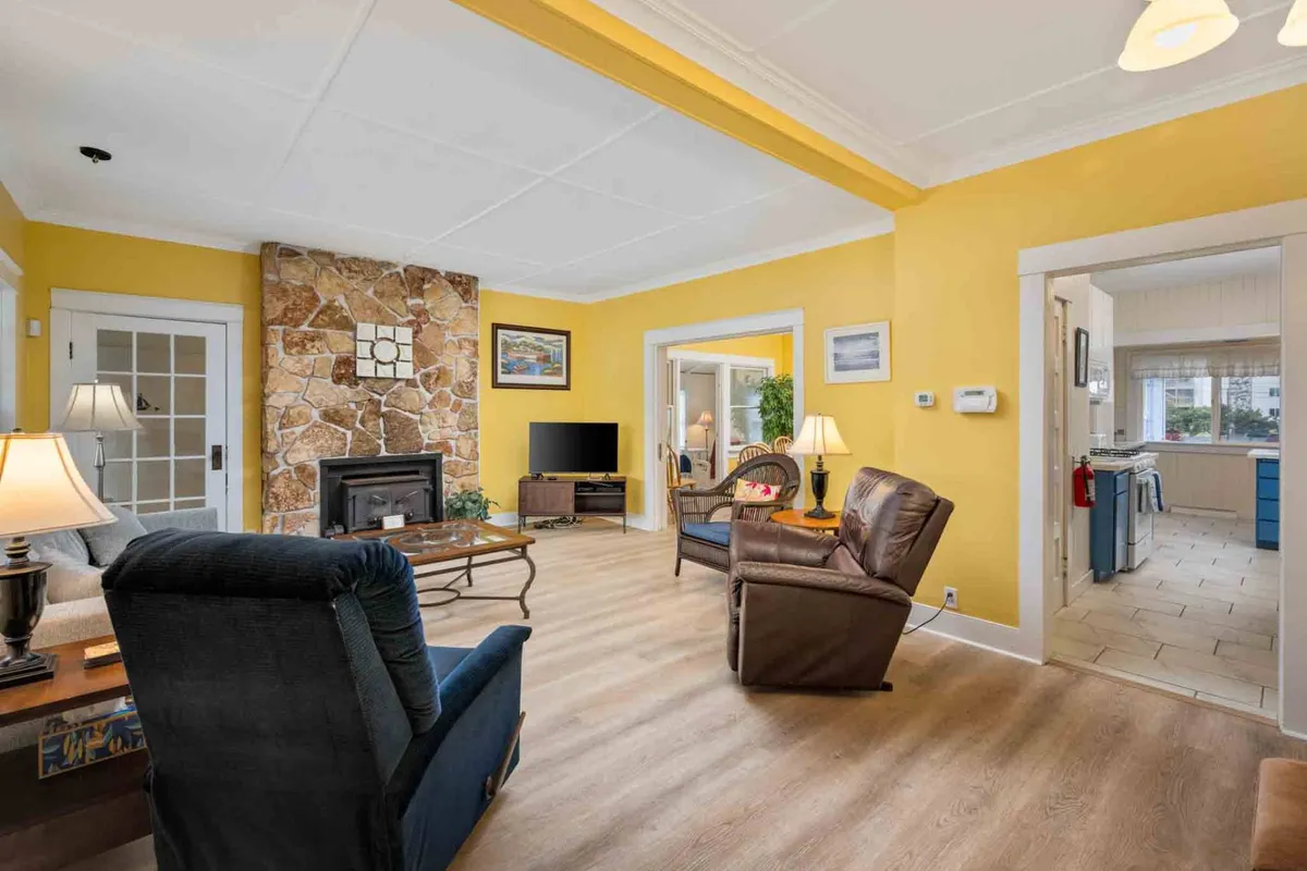 A warm, inviting living room featuring a stone fireplace, yellow walls, comfortable seating, and a television. The arrangement encourages socializing and relaxation, with thoughtful decor and cozy details like soft lighting and plush seating.