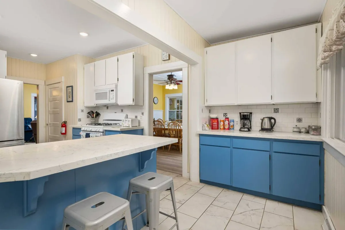 The kitchen’s island countertop is the focal point in this image, complemented by blue cabinetry and sleek stainless steel appliances. The open-concept design shows the dining area in the background, highlighting the connection between meal prep and family dining. The scene evokes warmth and togetherness.
