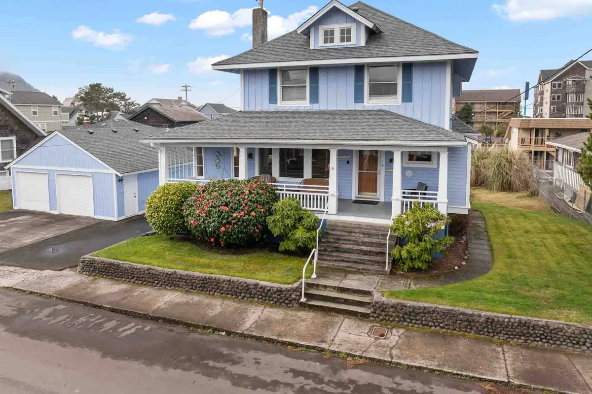 A cheerful exterior view of a blue house with a welcoming front porch, surrounded by a well-maintained garden. The inviting porch seating and open yard suggest a perfect home base for easy access to the neighborhood and a relaxing return from downtown adventures.