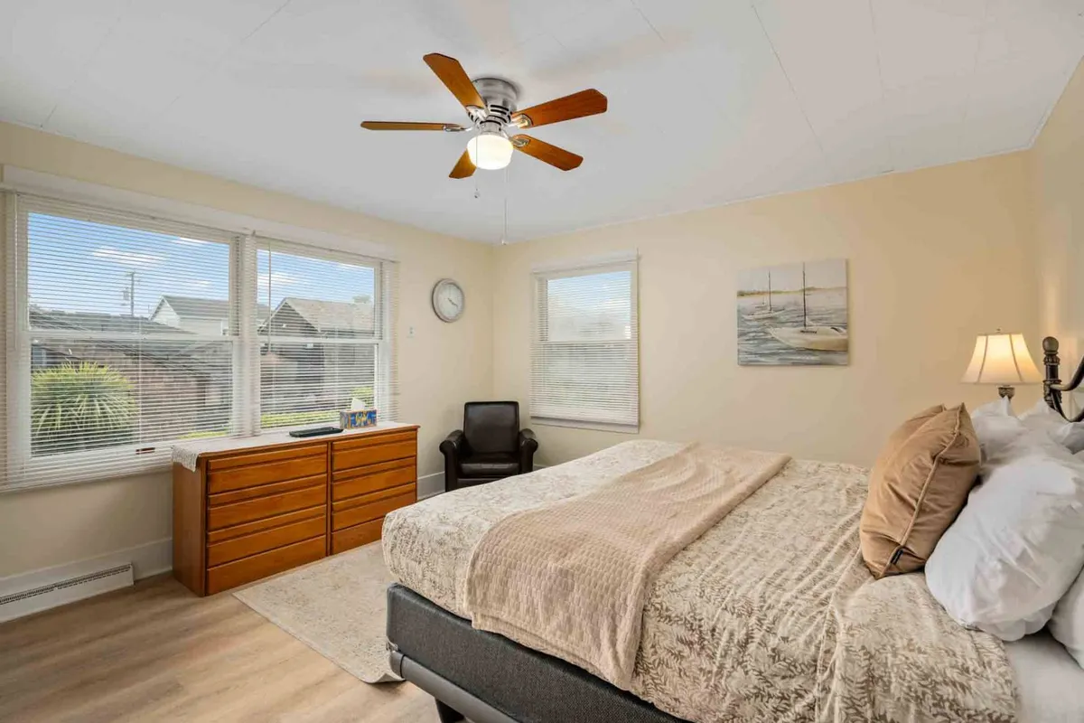 A comfortable bedroom featuring a bed, a dresser, a window offering serene views, and a sitting area perfect for reading or enjoying morning coffee. Natural light fills the room, enhancing its welcoming atmosphere.