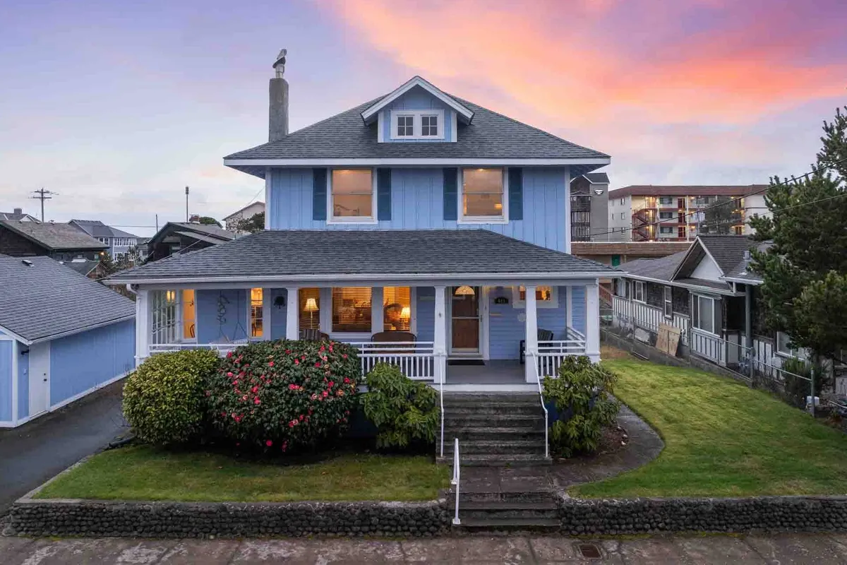 This image features the charming blue facade of Roxie's Retreat, complete with a welcoming front porch and lush garden greenery. The porch is ideal for relaxing or gathering with family, establishing an inviting first impression that resonates with the home's cozy and family-friendly atmosphere.