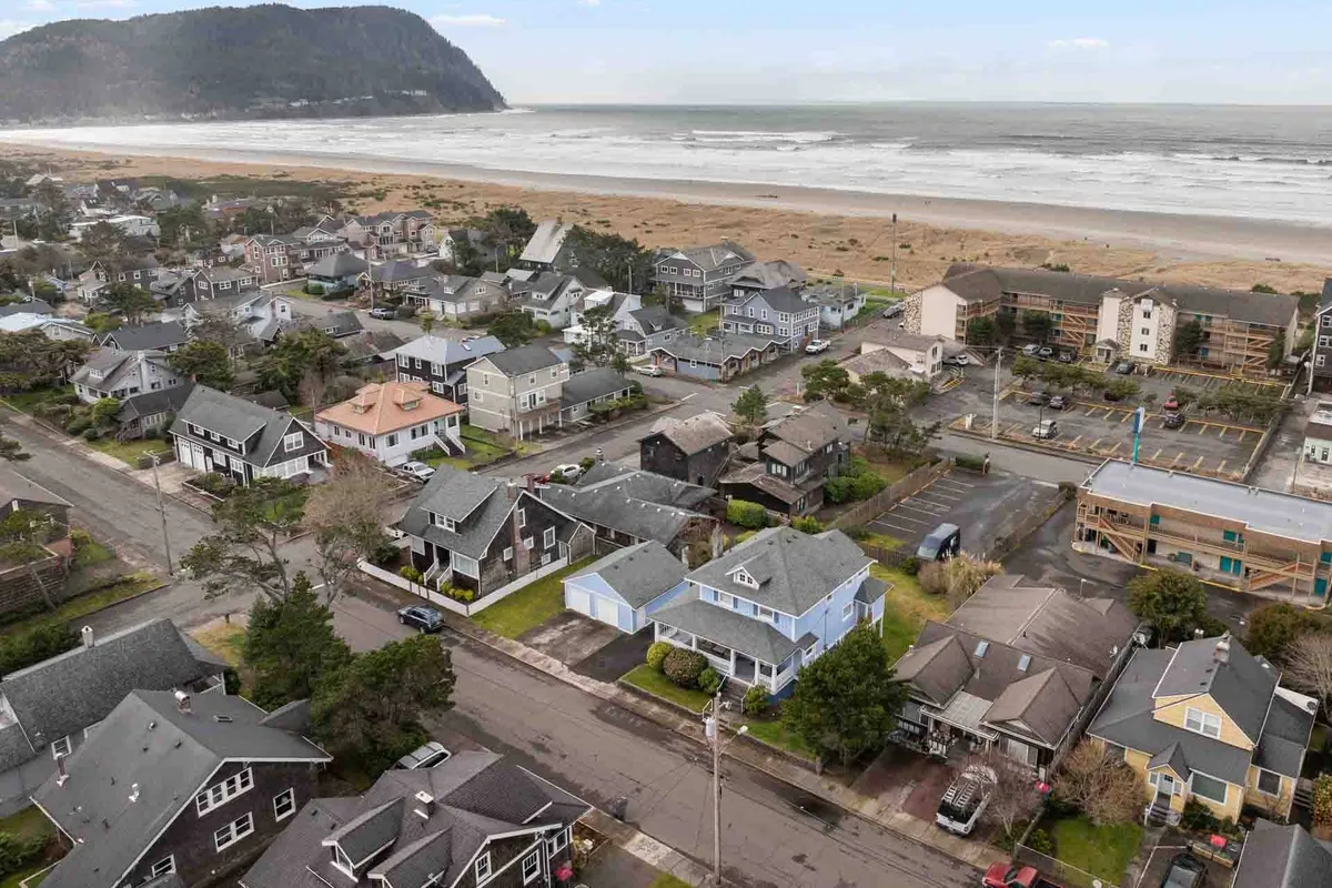A scenic perspective showing colorful houses nestled close to a sandy shoreline, with the expansive beach, rolling ocean, and a distant mountain backdrop. The image hints at both community life and access to outdoor activities.