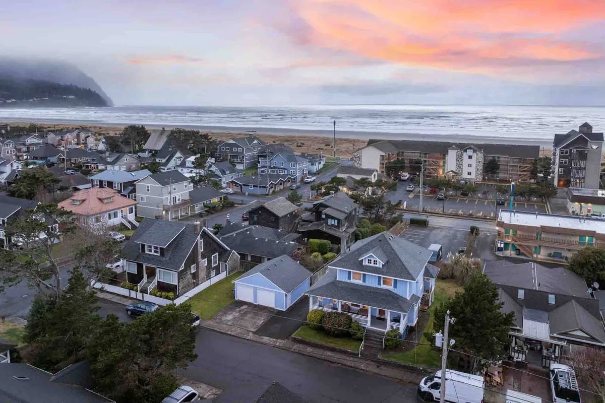An elevated view over a quiet neighborhood toward the ocean, with sunset colors spilling across the sky. The layout highlights a tranquil residential area with direct access to the beach and showcases the peaceful ambiance just minutes from Roxie’s Retreat.