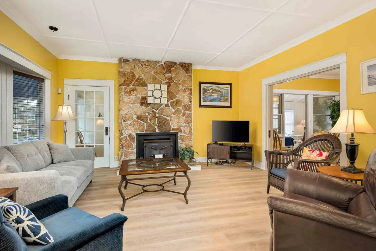 The image showcases a warm and inviting living room with cheerful yellow walls, a beautiful stone fireplace as the centerpiece, cozy seating arranged for conversation or relaxation, a stylish coffee table, and tasteful artwork. The overall mood is comfortable and welcoming, perfect for gathering with family or friends after a day at the Oregon coast.