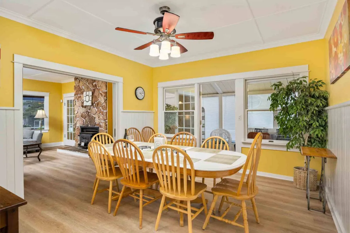 A spacious dining area with a wooden table, yellow walls, and a ceiling fan overhead. The table is set up for family meals or friendly gatherings, and the environment feels warm and welcoming, ideal for both everyday breakfasts and special celebrations.